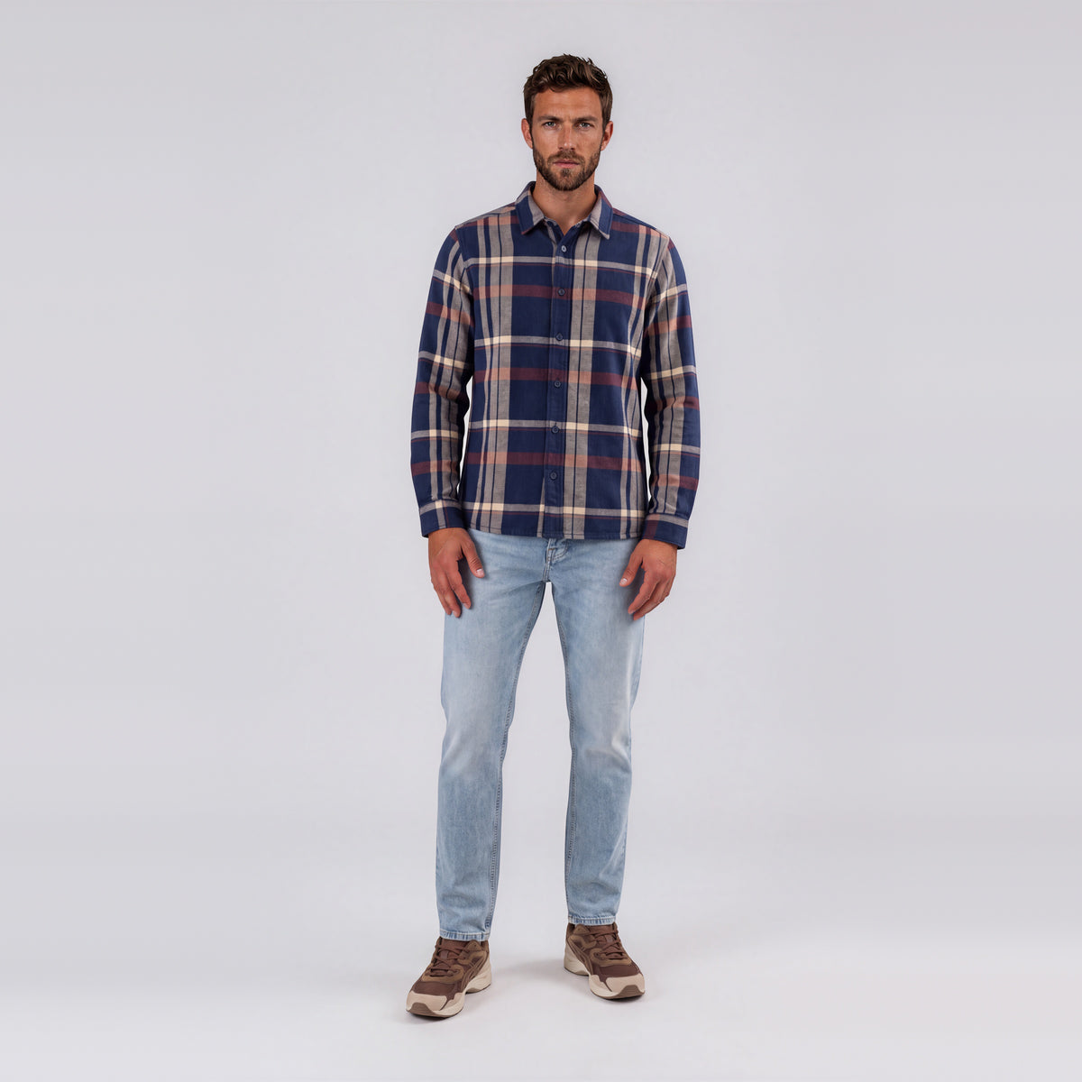 Man wearing Garment Works Tex check shirt in navy, cream and rust with light wash jeans
